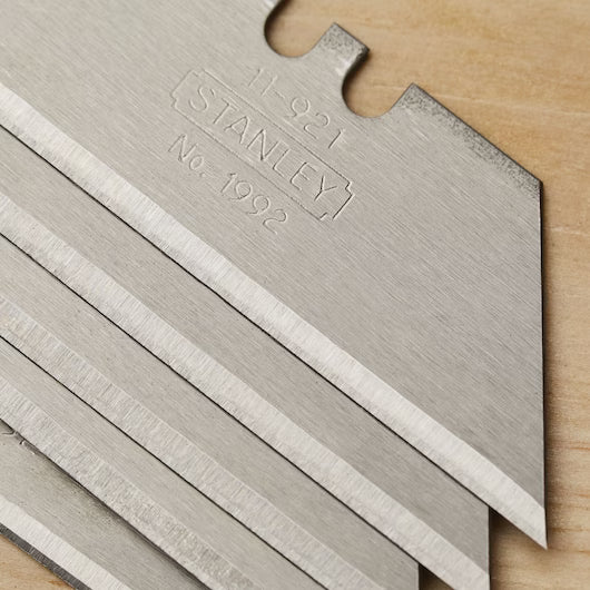Close-up of stacked STANLEY 1992® Heavy-Duty Utility Blades (5 PK) with sharp, angled edges on wood, featuring engraved STANLEY No. 1992 on the top blade.