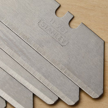 Close-up of several overlapping STANLEY Rounded Tip Blades (5 pc) with sharp edges for precision cutting, placed on a wooden surface.