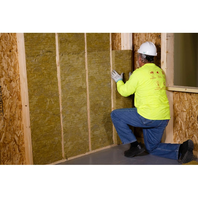 A construction worker in a yellow shirt and hard hat installs Owens Corning R15 Thermafiber Fire and Sound Guard 15 in. x 47 in. Mineral Wool Insulation Batts between wall studs for improved noise control.
