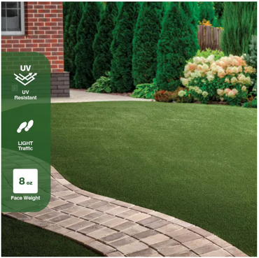 A landscaped yard features the TrafficMaster Emerald Green Precut Turf 6 ft. x 8 ft. Artificial Grass Rug, with a curved stone path and bushes by a brick house. Icons show UV resistance, light traffic suitability, and 8 oz face weight.