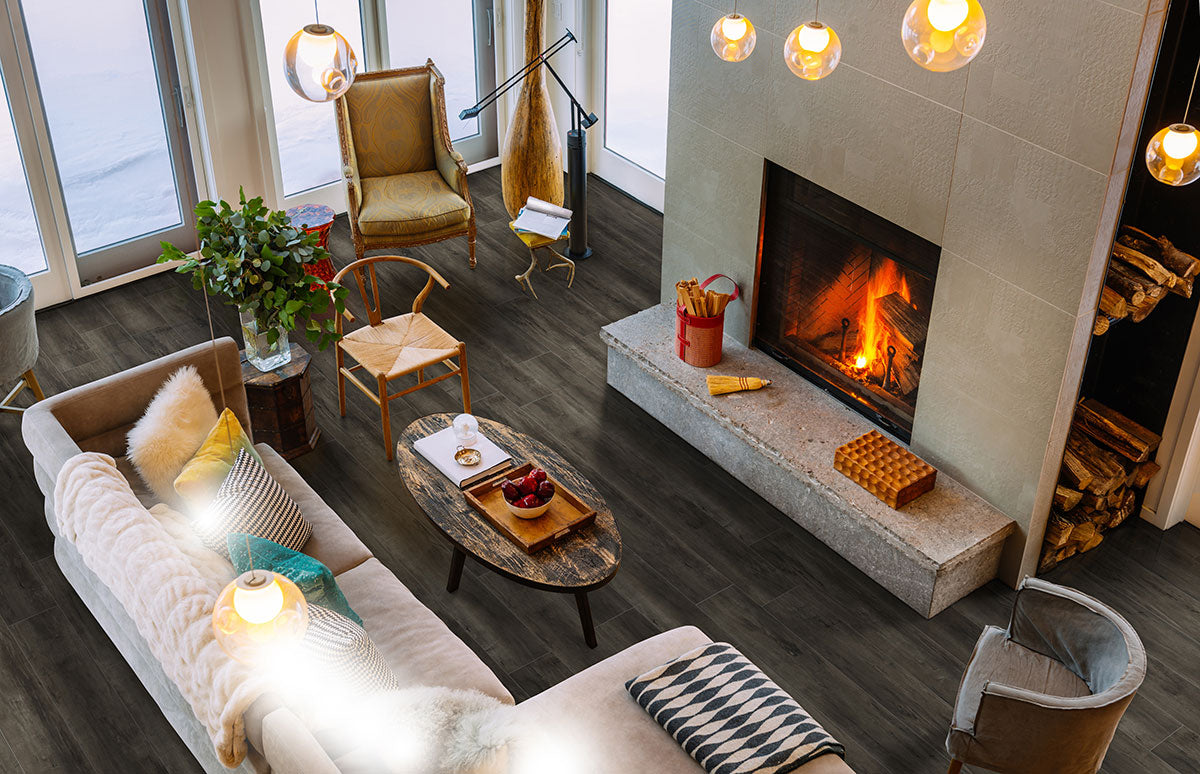 A cozy living room with a lit fireplace, modern furniture, beige sofa, Cyrus Billingham Luxury Vinyl Planks by MSI featuring waterproof SPC core and easy click-lock installation, wooden coffee table, large armchair, tall windows, and stacked logs nearby.