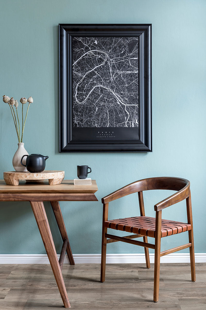 A modern interior features a wooden tea table, leather-seated chair, and abstract map art on pale blue walls—all set atop MSIs Cyrus Draven Luxury Vinyl Planks BOX (23.77 SQFT) flooring, designed for lasting style and durability.