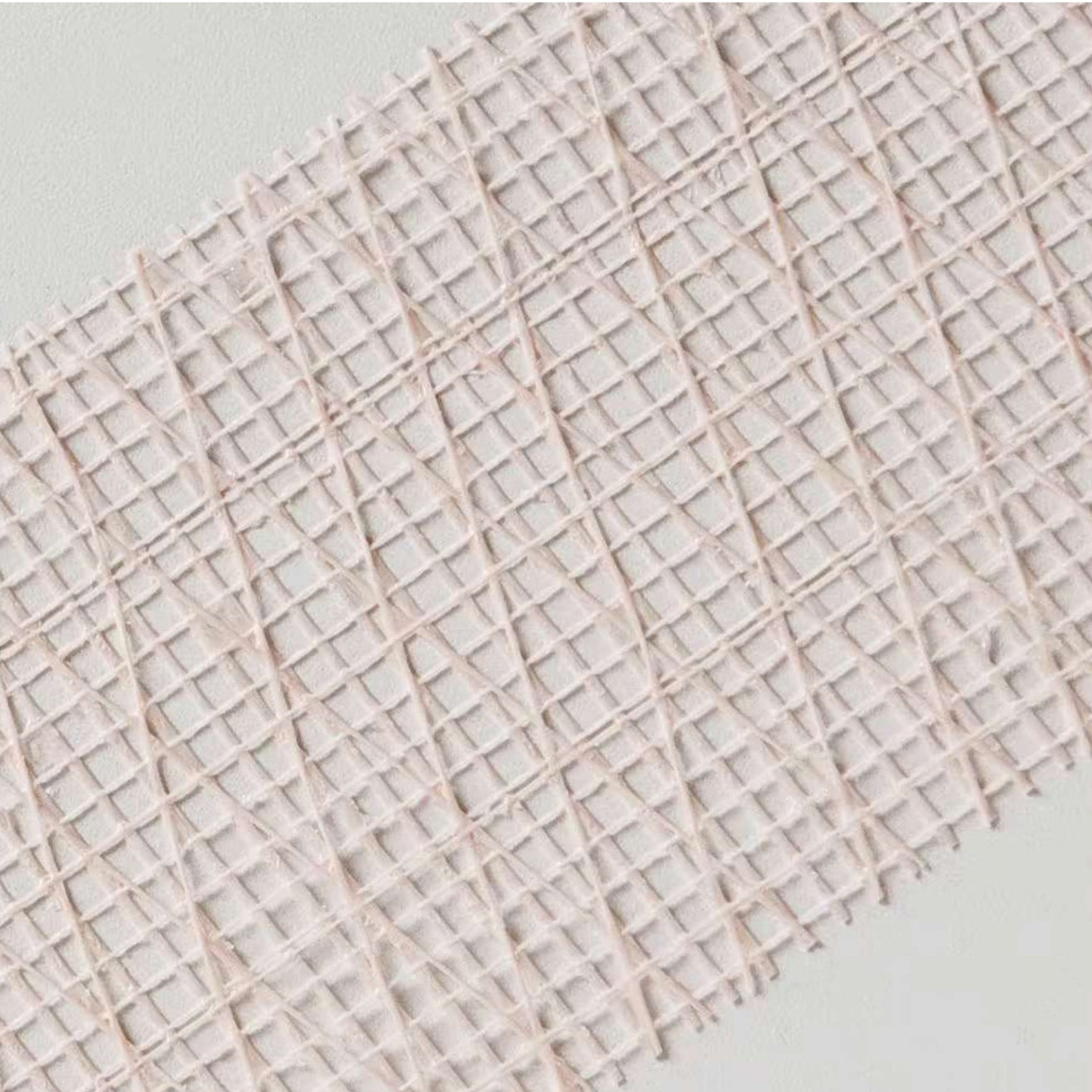 A close-up of ADFORS FibaTape FDW8666-U 2-3/8 in. x 250 ft. Extra Strength Reinforced Drywall Tape with a crisscross grid pattern in light pink, shown diagonally on a light grey surface, perfect for drywall seam reinforcement.