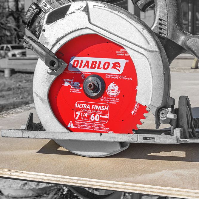 A 7-1/4 in., 60-teeth Diablo D0760A Ultra Finish saw blade featuring TiCo Hi-Density carbide is on a wooden board outdoors, with sunlight casting shadows and blurred structures in the background.