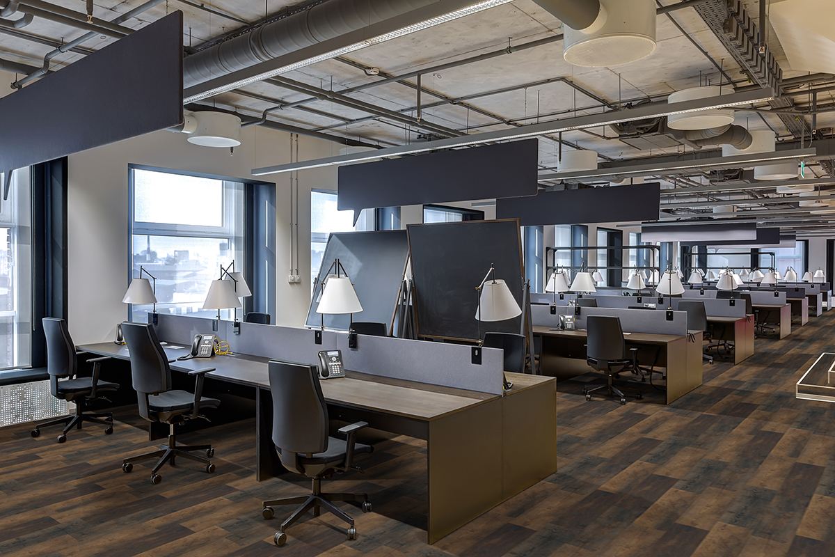 A modern open-plan office with rows of desks, chairs, and lamps features MSI Cyrus Hawthorne Luxury Vinyl Planks (23.77 SQFT/box) with a CrystaLux™ wear layer. Large windows and exposed ceilings create an industrial yet organized atmosphere.