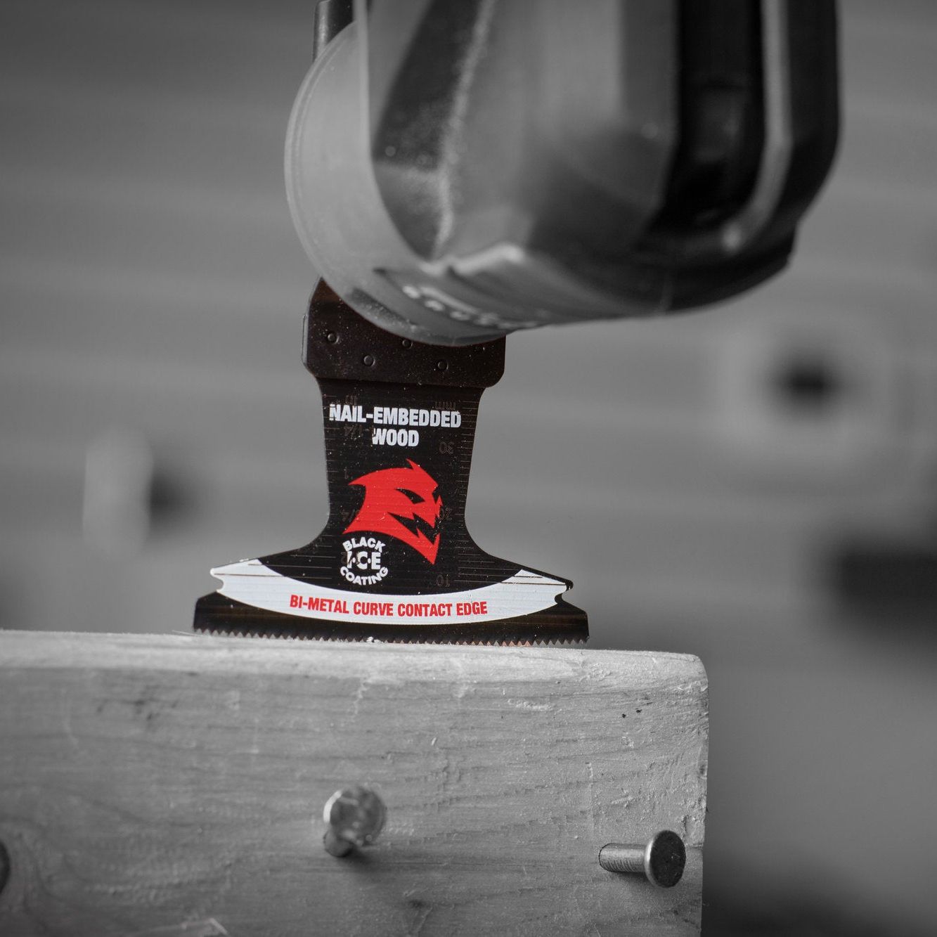 Close-up of the DIABLO DOU250BW3 Demo Demon™ blade marked for NAIL-EMBEDDED WOOD with BI-METAL CURVED CONTACT EDGE cutting wood. The blade, featuring an ultra-hardened cutting edge and a red stylized head logo, is in focus against a blurred grayscale background.