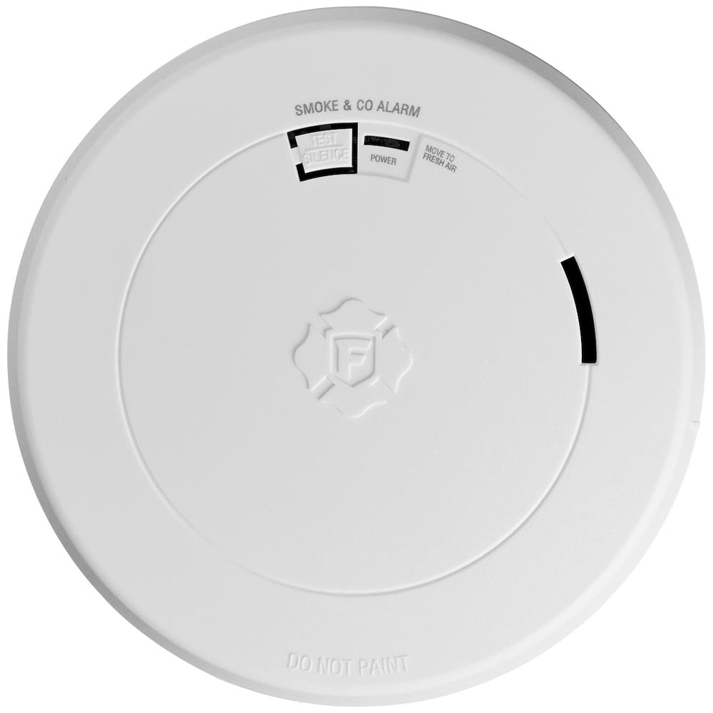A round, white FIRST ALERT 1046796 SMCO210 smoke and CO alarm features a 10-year battery, test button, power indicator, slim profile, instruction label, side vent, and “DO NOT PAINT” marking.
