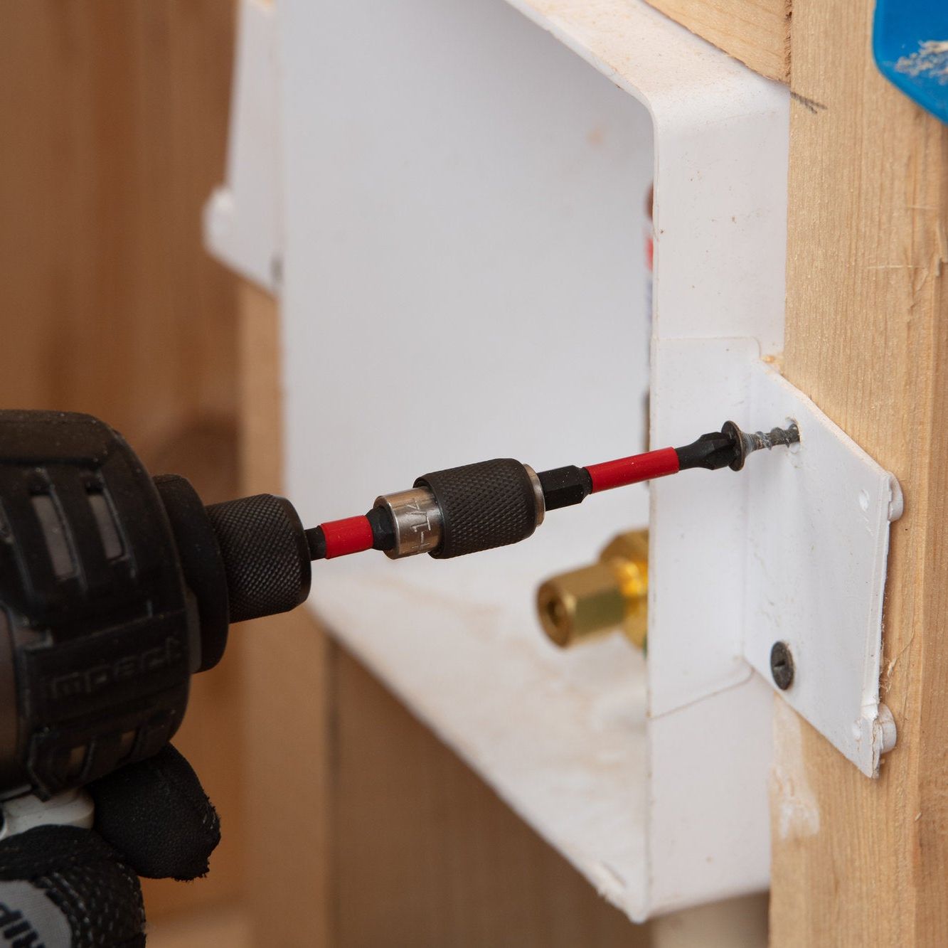 A person wearing gloves uses a cordless drill with a DIABLO DPH11P5 1 in. #1 Phillips bit to drive a screw into white metal on wooden planks, with a blue electrical box in the background demonstrating the power of the MaxTorque Zone.