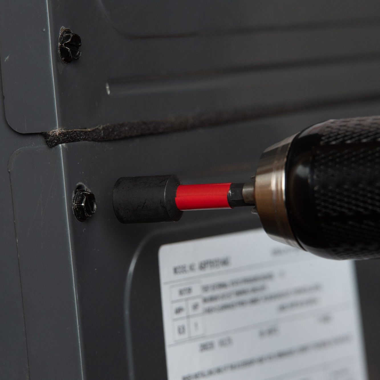 Close-up of a Diablo DIABLO DNTSL12 1/2 in. x 2-9/16 in. Magnetic Nut Driver, featuring Impact Strong™ technology, tightening a black screw into gray metal with a partially visible label.