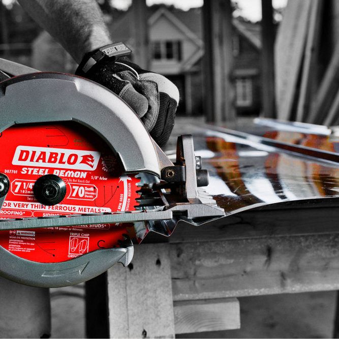 A person at a construction site with wooden beams uses a Diablo Steel Demon™ blade, a vivid red D0770FA 7-1/4 in. x 70 teeth carbide-tipped circular saw blade, featuring Triple Chip Grind, on metal against a grayscale background.