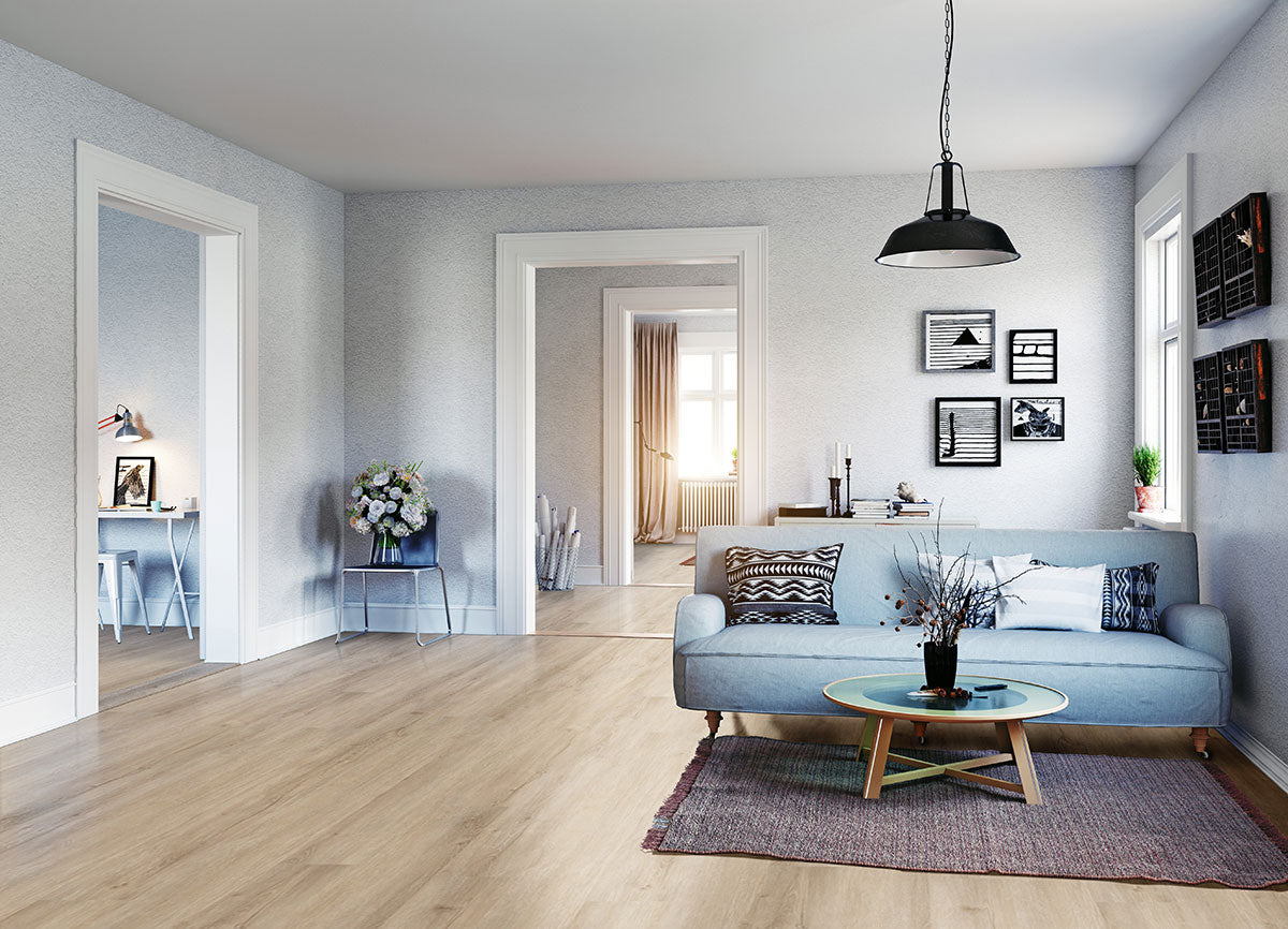 Bright living room with MSI XL Cyrus Sandino Luxury Vinyl Planks (22.44 SQFT/box), blue sofa, round glass coffee table, wall art, and a black hanging lamp. Doorways show a workspace and sunlit room in back.