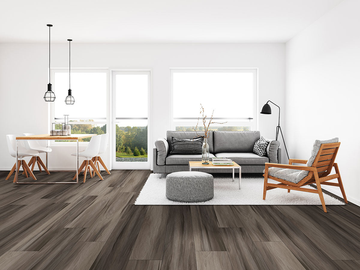 Modern living and dining area with large windows, gray sofa, wooden armchair, round ottoman, dining table with chairs, pendant lights, white walls, and MSI XL Cyrus Jenta Luxury Vinyl Planks featuring a 100% waterproof click-lock system.