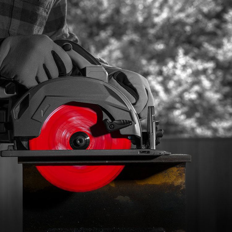 Wearing gloves, a person uses the DIABLO D0748CFA 7-1/4 in. x 48-Teeth Steel Demon™ Cermet II saw blade by Diablo to easily cut through dark metal, the bright red blade enhancing precision. The saw, angled dynamically against the blurred background, demonstrates exceptional metal-cutting action.