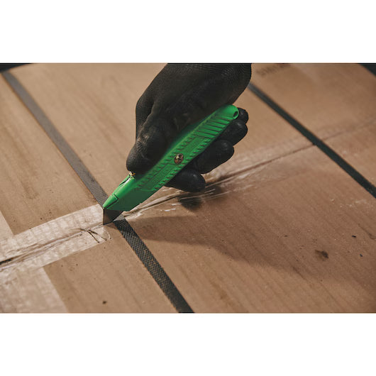 A hand in a black glove uses the STANLEY® Hi-Visibility Retractable Knife to cut clear packing tape on a cardboard box held with black straps.