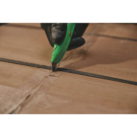 A gloved hand uses the STANLEY® Hi-Visibility Retractable Knife to cut brown cardboard packaging secured with a black plastic strap.