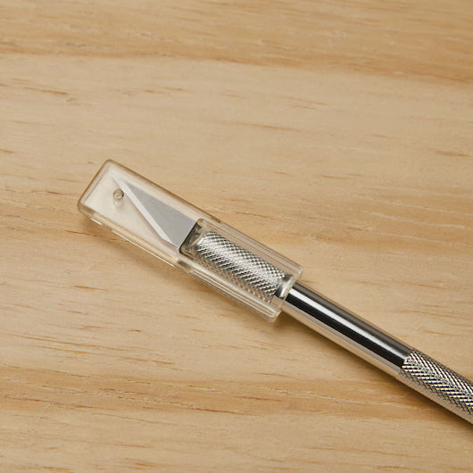 The STANLEY Hobby Knife, featuring a textured metal handle, replaceable blades, and a clear plastic safety cap, rests on a light wooden surface.