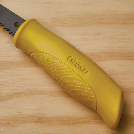 Close-up of a yellow STANLEY® Jab Saw, 6TPI handle with a textured grip on wood, attached to a black serrated blade, partially visible at the top left.