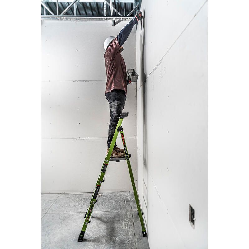 A construction worker in a hard hat uses the LITTLE GIANT 15396-001 MightyLite IA 6 ft. 300 lb. rated fiberglass stepladder to install drywall in an unfinished room, reaching toward the ceiling with tools.