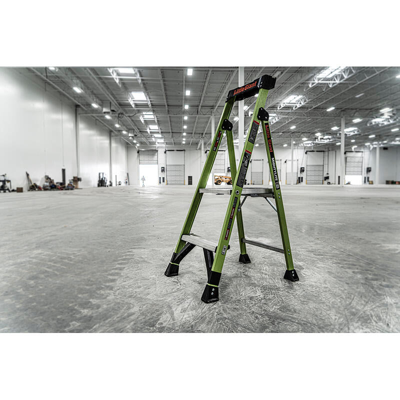 A LITTLE GIANT 15394-001 MightyLite IA 4 ft. fiberglass stepladder, rated for 300 lbs., stands open in a brightly lit, spacious industrial warehouse with high ceilings.