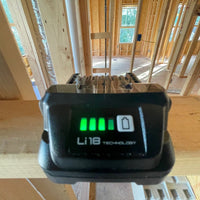 Close-up of a Metabo HPT 377797M BSL1820M 18V 2.0Ah Lithium Ion Battery with Fuel Gauge by Go Build, The Fastest Way To Build, showing three green charge bars on a wooden beam in a house under construction with exposed framing and windows.