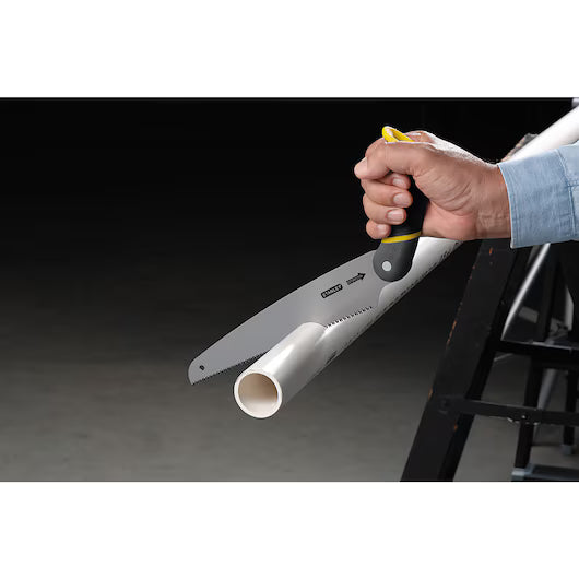 A hand uses the STANLEY 3-in-1 Multi-Purpose Saw to cut a white PVC pipe resting on a black sawhorse, set against a dark background.