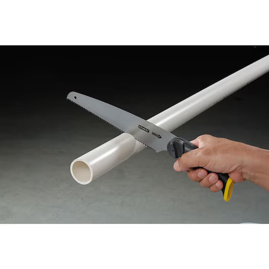 A hand wields the STANLEY 3-in-1 Multi-Purpose Saw to cut through a white plastic pipe against a dark background.