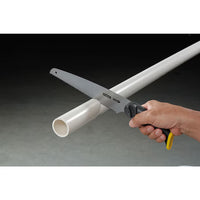 A hand wields the STANLEY 3-in-1 Multi-Purpose Saw to cut through a white plastic pipe against a dark background.
