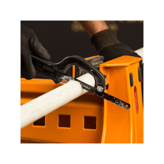 Wearing black gloves, a person uses the STANLEY® Mini Hacksaw to cut a white plastic pipe secured on an orange workbench, illustrating the tools precision and efficiency for cutting tasks.