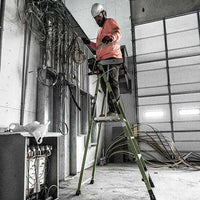 A construction worker in a hard hat and hi-vis jacket stands on the LITTLE GIANT 19304 FORTRESS IAA 4 Fiberglass Platform Ladder with Wraparound, managing electrical wires inside an unfinished building—ideal for professional contractors.