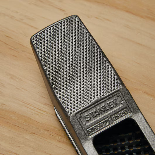 Close-up of a STANLEY® SURFORM FLAT FILE - REGULAR CUT 10IN (250MM) by STANLEY, featuring a textured, crisscross-patterned surface and branding—perfect for precise woodworking on a wooden surface.