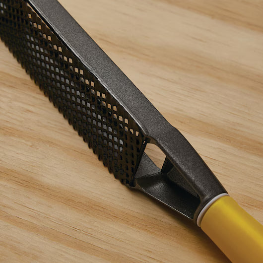 A close-up of the STANLEY® SURFORM FLAT FILE - REGULAR CUT 10IN (250MM) with a yellow handle on wood, highlighting its textured blade—a versatile STANLEY tool for woodworking.