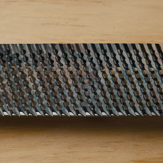 Close-up of the STANLEY® SURFORM FLAT FILE - REGULAR CUT 10IN (250MM) by STANLEY, showing its sharp, raised teeth and textured surface designed for woodworking and shaping a variety of materials, set on a light wooden background.