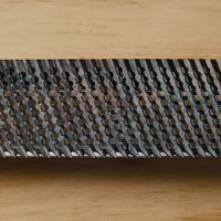 Close-up of the STANLEY® SURFORM FLAT FILE - REGULAR CUT 10IN (250MM) by STANLEY, showing its sharp, raised teeth and textured surface designed for woodworking and shaping a variety of materials, set on a light wooden background.