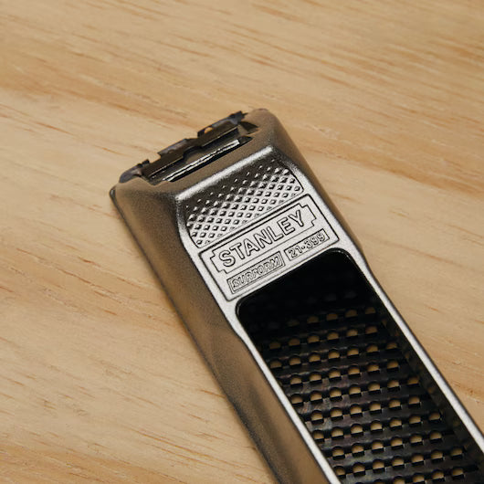 Close-up of a STANLEY 6 IN SURFORM® POCKET PLANE on wood, featuring its textured handle, metal body, and grated blade—an essential tool for shaping or smoothing materials in woodworking.