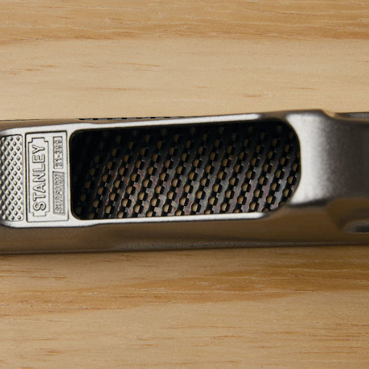 Close-up of a STANLEY 6 IN SURFORM® POCKET PLANE, a versatile tool with a textured, gridded surface and engraved branding, resting on light wood.