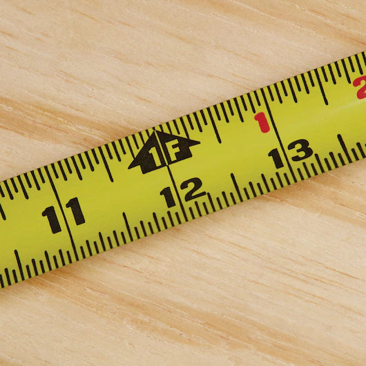 A close-up of the STANLEY 25 ft PowerLock® Tape Measure, a durable yellow tool on wood, displays measurements from 11 to 13 inches with a “1F” foot marking.