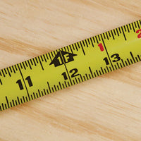 A close-up of the STANLEY 25 ft PowerLock® Tape Measure, a durable yellow tool on wood, displays measurements from 11 to 13 inches with a “1F” foot marking.