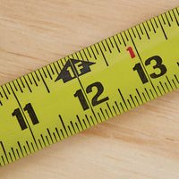 Close-up of the 25 ft STANLEY® FATMAX® Classic Tape Measure by STANLEY, with its yellow blade extended from 11 to 14 inches across a wooden surface.