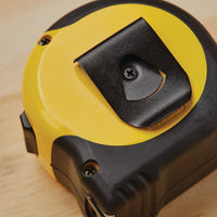 A close-up of the STANLEY 25 ft FATMAX Classic Tape Measure, featuring a yellow and black design with a metal belt clip, resting on light wood. This durable tool from STANLEY ensures precise measurements for any project.