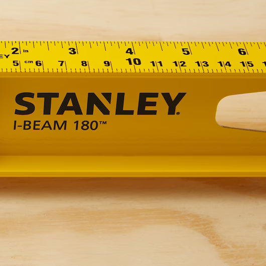 A close-up of a yellow STANLEY 24 in 180° I-Beam Level, a dependable construction tool, resting on wood with black measurement markings and a cutout handle.