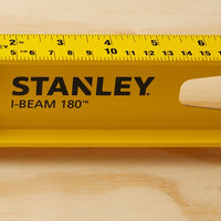 A close-up of a yellow STANLEY 24 in 180° I-Beam Level, a dependable construction tool, resting on wood with black measurement markings and a cutout handle.