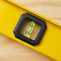 A close-up of a yellow STANLEY 48 in I-Beam 180 Level on wood, with the bubble centered between two lines—a professional-grade tool perfect for construction projects.