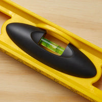 A close-up of the STANLEY 24 in High-Impact ABS Level on wood, featuring a green liquid-filled vial and a black grip handle.