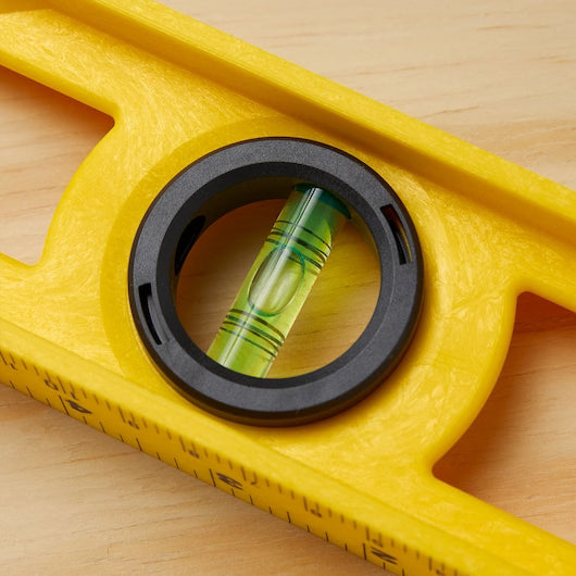 Close-up of the STANLEY 24 in High-Impact ABS Level, featuring a central bubble vial accurately aligned between black lines—ideal for reliable horizontal checks on a light wood surface.