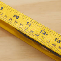 Close-up of a yellow tape measure showing 9-13 inches on wood, with the STANLEY 24 in High-Impact ABS Level nearby—ideal for accurate measuring and leveling tasks.