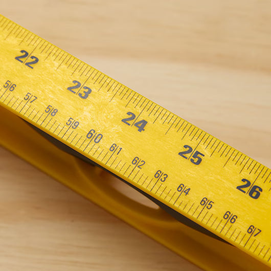 Close-up of a yellow measuring tape showing 22-25 inches on light wood—ideal for use with your Go Build STANLEY® ABS I-Beam Level 1200mm for precise projects.