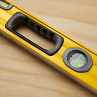 The STANLEY® FATMAX® Aluminum Box Beam Level 1200mm, featuring a black handle and two bubble vials for horizontal and vertical alignment, rests on a light wooden surface.