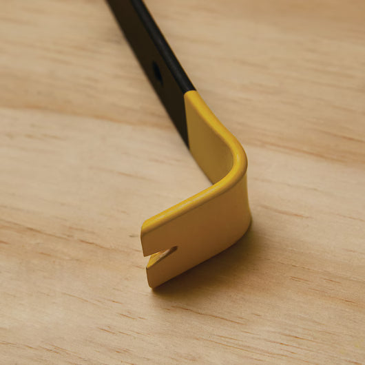 A close-up of the yellow, angled end of the STANLEY 7 IN WONDER BAR® II PRY BAR, a compact, precision-forged steel tool with a slot, resting on a light wooden surface.