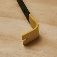 A close-up of the yellow, angled end of the STANLEY 7 IN WONDER BAR® II PRY BAR, a compact, precision-forged steel tool with a slot, resting on a light wooden surface.
