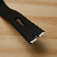 Close-up of the metal end of a STANLEY® STEEL FLAT WONDER BAR® - 15IN / 380MM, featuring a notched, flat tip and beveled edge, resting on a light wooden surface.